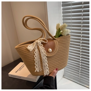 Close-up of woven straw tote bag with brown leather flap, pearl button, and beige lace ribbon