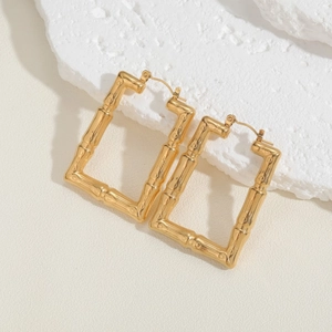 Macro detail of gold square bamboo texture earrings on white textured stone background