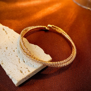 Macro shot of double-layer gold bangle with zircon pavé on white stone and satin
