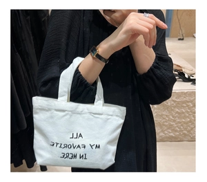 Detailed close-up of a white canvas tote bag with black slogan print held by a model
