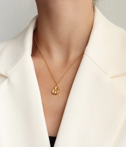 Polished gold teardrop pendant necklace worn at the collarbone with a minimalist style