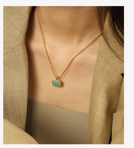 Detail of a gold rice chain necklace with a green amazonite pendant on a model