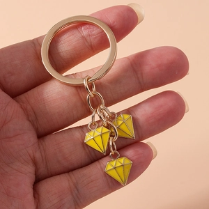 Detail of hand holding golden keychain with three yellow enamel diamond charms