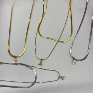 Detailed view of gold and silver flat snake chains with crystal letter pendants