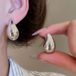 Macro detail of silver C-shaped teardrop earrings with a polished metallic finish on a model