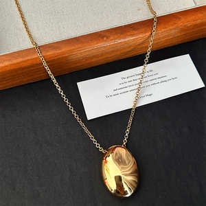 Detail of a shiny gold oval pendant necklace resting on a wood tray and black surface