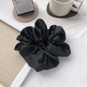 Macro detail of oversized black satin scrunchie with silky pleated texture on white desk