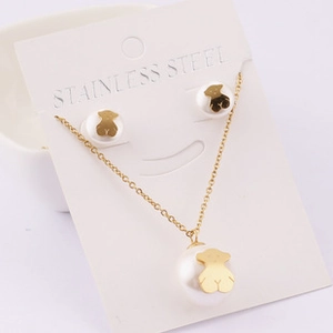 Detail of stainless steel necklace and earrings set featuring white beads and gold bears