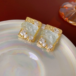 Dettaglio macro di orecchini quadrati placcati in oro con cristallo verde e zirconi
