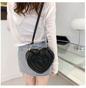 Detail showing a stylish heart-shaped black leather crossbody bag worn by a model