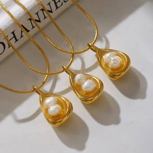 Three golden snake chains with unique shell pendants and pearls on marble surface