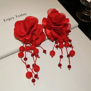 Detail of red flower earrings with matching bead tassels on a decorative book background
