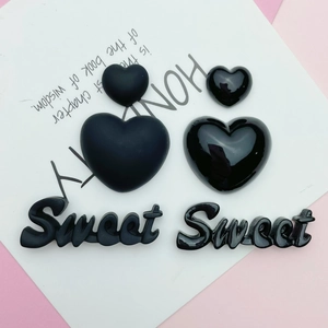Flat lay of black resin heart and Sweet letter charms in matte and glossy finishes