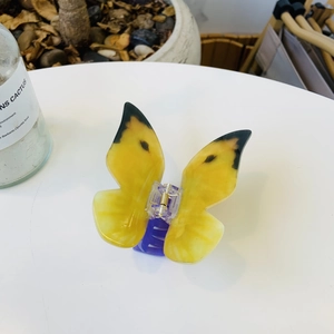 Detail of a translucent yellow acrylic butterfly hair claw with purple grip on a table