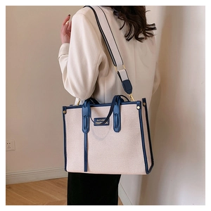 Detail of contrast canvas tote bag with dark blue leather trim and wide shoulder strap