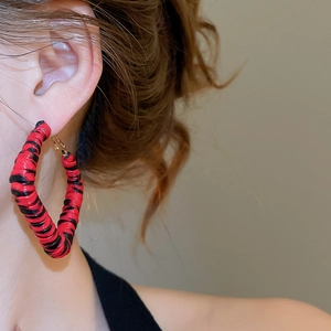 Détail de grandes créoles avec texture léopard en spirale rouge et noire entrelacée