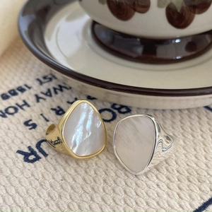 Close-up of silver and gold mother of pearl shell rings on a beige woven fabric surface