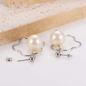 Close-up of white pearl stud earrings with a hollow silver flower metal frame design