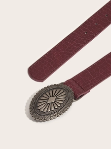 Detail of burgundy crocodile pattern leather belt with embossed silver oval buckle
