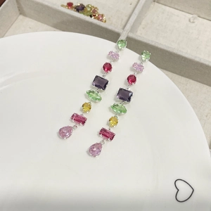 Macro detail of silver drop earrings with colorful crystals and fringe on ceramic tray