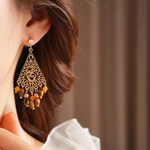 Close-up of golden geometric earrings with brown beads worn on a female model