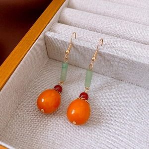Detailed view of handmade persimmon earrings with green and orange beads in a jewelry box