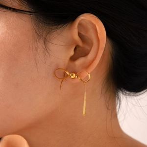 Close-up of 18k gold butterfly bow stud earrings with chain tassels worn on ear