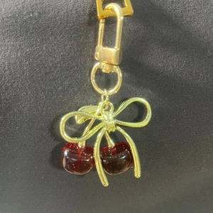 Close-up of a realistic red cherry pendant with golden bow on a metal keychain