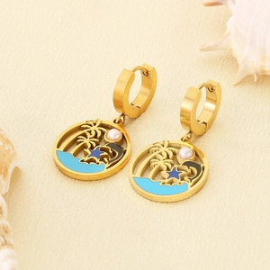 Detail of gold dolphin earrings with tropical palm tree design and blue enamel sea wave texture
