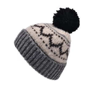 Détail du bonnet en tricot montrant le motif jacquard et le pompon noir en fausse fourrure