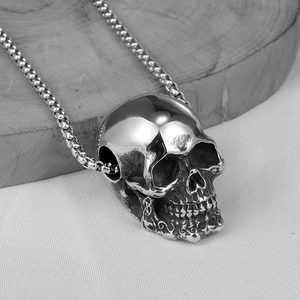 Macro shot of polished skull pendant and round link chain on wooden base in black and white