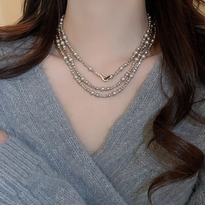 Détail d'un collier à perles argentées avec fermoir doré sur un pull gris chiné