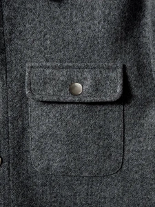 Detail of dark grey textured wool jacket featuring flap pocket and matte metal button