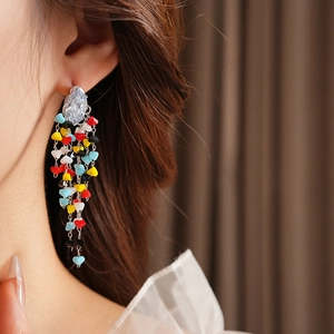 Close-up of dangling silver earrings with colorful beads on a model's ear