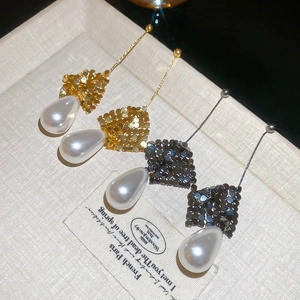 Macro shot of gold and silver drop pearl earrings with mesh texture on beige background