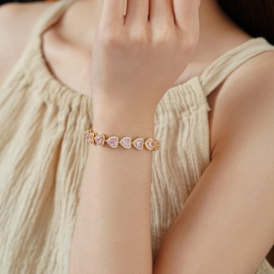 Close-up of pink heart zircon bracelet on a model's wrist with golden double chains