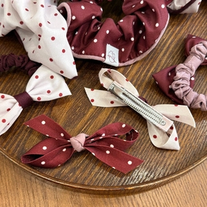 Polka dot hair accessory set with burgundy scrunchies and bow clips on a wooden tray