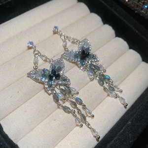 Gros plan détaillé des boucles d'oreilles papillon avec cristaux bleus et pompons argentés