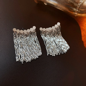 Detail showing silver metallic chain tassels on minimalist earrings over leather background