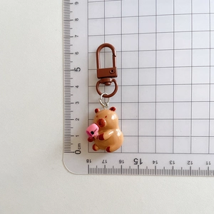 Detail view of a brown Capybara keychain with pink accessory next to a ruler for size