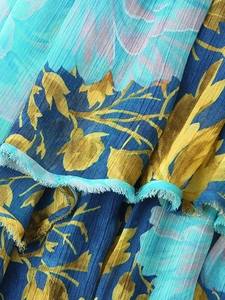 Detailed macro view of teal chiffon fabric with yellow floral print and fringe edges