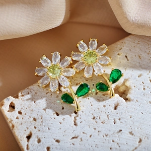 Close-up of gold-plated daisy earrings with green leaf stones and sparkling zircons