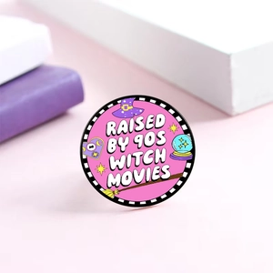 Detailed view of pink enamel horror movie badge with Raised by 90s Witch Movies text