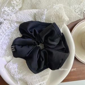 Détail d'un chouchou fait main en satin de soie noir avec broderie dorée sur plateau