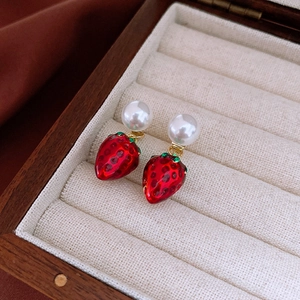 Detailed macro view of red strawberry enamel earrings with white pearls in a wooden box