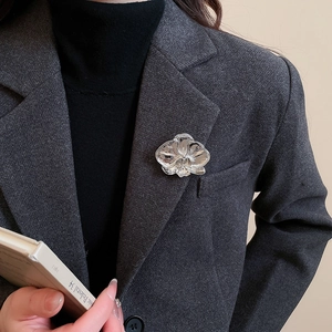 Detail of silver orchid brooch featuring artistic petal texture on a grey wool blazer