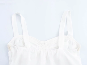 Détail des bretelles du crop top blanc et de la texture du tissu sur fond plat blanc