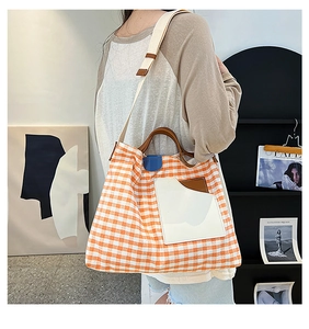 Detail of a large canvas tote bag with orange checkered pattern and leather handles