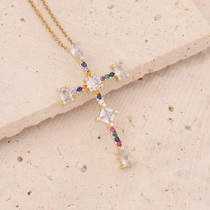 Macro detail of 18K gold cross pendant with colorful zircon stones on stone background