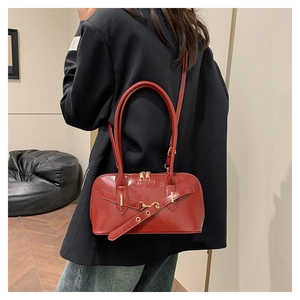 Chic red patent leather baguette bag with gold hardware shown on shoulder of model
